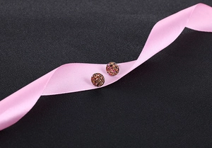 Macro detail of round crystal cluster earrings on pink silk ribbon over black background