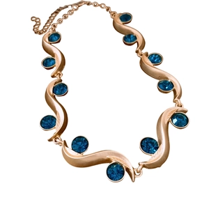 Elegant gold necklace with a round blue gemstone in a wave design on white background