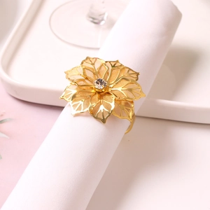 Close-up of golden hollow flower napkin ring with a sparkling crystal center on a white cloth