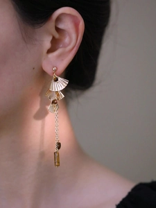 Détail de boucles d'oreilles à pompons avec feuilles de ginkgo dorées et perles oeil de tigre