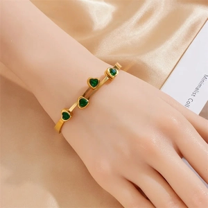 Gold plated open bangle featuring four green heart-shaped zircon stones on silk background