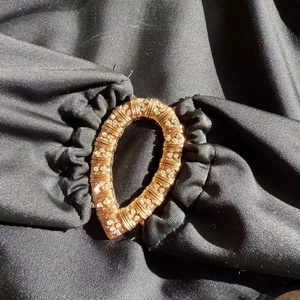 Macro detail of golden crystal-encrusted buckle on pleated black one-piece swimsuit