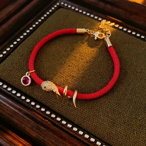 Macro shot of red braided rope bracelet with gold snake charm and ruby gemstone detail