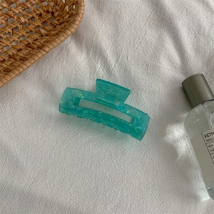 Macro detail of translucent turquoise hair claw clip with marble texture on white fabric