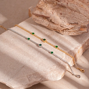 Elegant gold and silver link bracelets featuring emerald green zircons on stone background