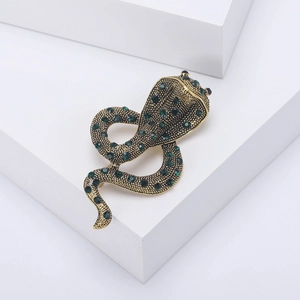 Macro detail of a vintage cobra snake brooch featuring green rhinestones on gold alloy