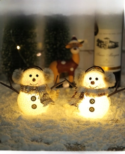 Detail of two glowing Christmas snowman lamps with plaid scarves and warm LED lighting