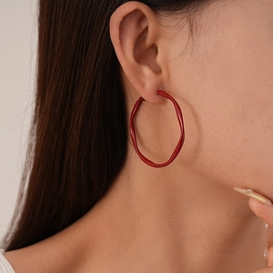 Close-up of model wearing vibrant red wavy hoop earrings in a minimalist style