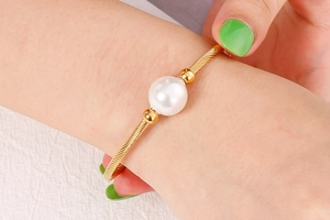 Détail macro du bracelet torsadé doré avec une grande perle blanche sur le poignet