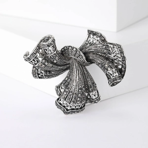 Vintage silver bow brooch with dark grey rhinestones on minimalist white display stand