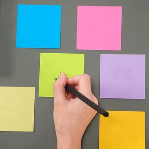 Primer plano de mano escribiendo en notas adhesivas fluorescentes de colores 3x3