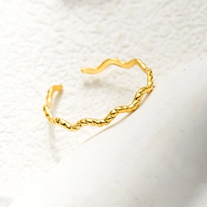 Macro shot of gold wave-patterned open ring showing the metallic texture and 18K finish