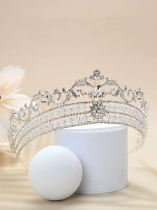 Detail shot of a silver bridal crown with sparkling rhinestones and white pearls on a pedestal