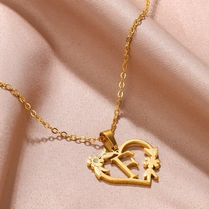 Dettaglio del ciondolo a cuore dorato con lettera F e decorazioni floreali