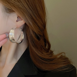 Detailed close-up of large textured silver hoop earrings featuring dual-texture finish