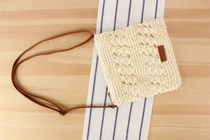 Detail of handwoven hollow straw bag with brown leather strap on light wood surface