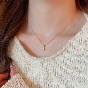 Primo piano di una delicata collana con ciondolo a stella dorata su un maglione bianco