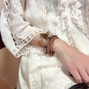Detail of bohemian multilayer beaded bracelet with brown tassels worn by a model