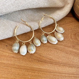 Detail shot of golden hoop earrings with natural shell pendants on a rustic wooden background