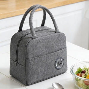Gray insulated lunch bag with wide handles and thick fabric on a white dining table
