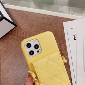 Yellow quilted leather phone case with card holder and gold chain strap held over desk