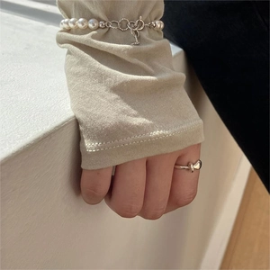 Detailed view of 925 sterling silver knot ring and pearl bracelet worn over beige sleeve