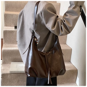 Detail of dark brown leather shoulder bag with decorative tassels and a small charm