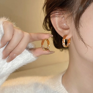 Elegant gold round earrings with orange and white zircon stones on model ear