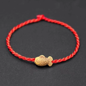 Detail view of a red woven rope bracelet with a carved yellow fish-shaped charm