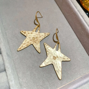 Close-up of star-shaped earrings with hammered metal texture in vintage matte gold