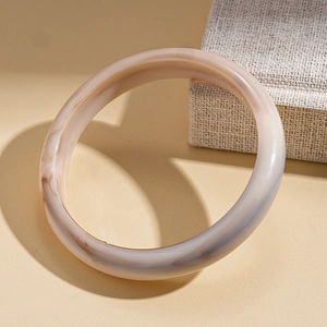 Detail view of acrylic bangle with beige marble texture on a textured surface