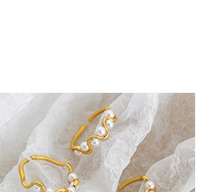 Detailed view of wavy gold-plated rings with multiple small white pearls on white fabric