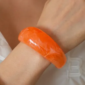 Detail of orange resin bangle with marble texture worn on wrist for a minimalist style