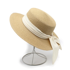 Detail view of woven straw sun hat with creamy ribbon bow and metallic button accent