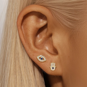 Detailed view of gold Hamsa hand and evil eye stud earrings with blue zircon on model ear