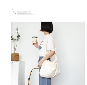 Side view of an off-white drawstring canvas hobo bag with a stylish pleated strap detail