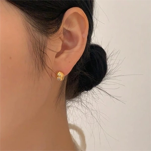 Close-up of gold irregular earring with liquid metal texture and zircon on a model