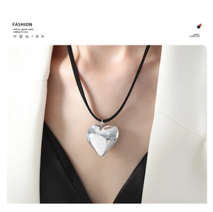 Close-up of a large polished silver heart pendant with a sleek black cord necklace