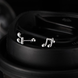 Macro shot of silver musical note stud earrings with threaded ball back on black surface