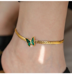 Close-up of a 18K gold-plated flat snake chain anklet with a green enamel butterfly pendant