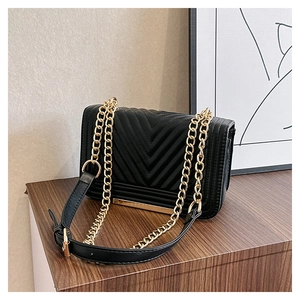 Detail of black chevron quilted shoulder bag with gold chain strap on a wooden stand