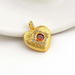 Detail of a gold heart pendant featuring a central red gem and white zircon accents