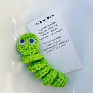 Handmade green crochet worry worm with a poem card for anxiety relief on a neutral surface