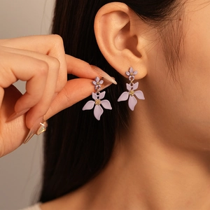 Boucles d'oreilles fleurs mauves avec détails dorés, portées par un mannequin