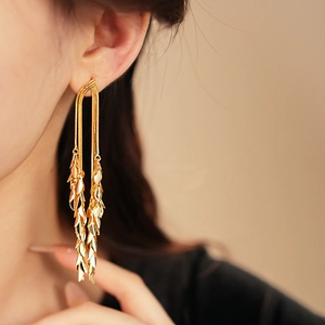 Close-up of elegant gold leaf tassel earrings worn by a model in warm lighting