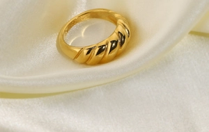 Detailed macro shot of a golden croissant dome ring resting on cream silk fabric