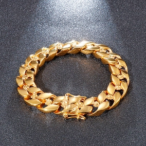 Macro detail of golden Cuban link bracelet featuring skull relief on dark matte background