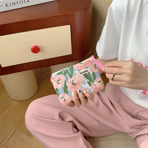 Floral makeup pouch with pink zipper and wrist strap held by person in cozy home setting