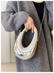 Close-up of a silver irregular oval clutch bag with thin metal chain strap on a model