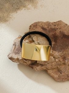 Close-up of a premium black elastic hair tie with a polished gold metal rectangular plate